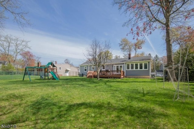 rear view of property with a wooden deck, a lawn, a playground, a chimney, and fence