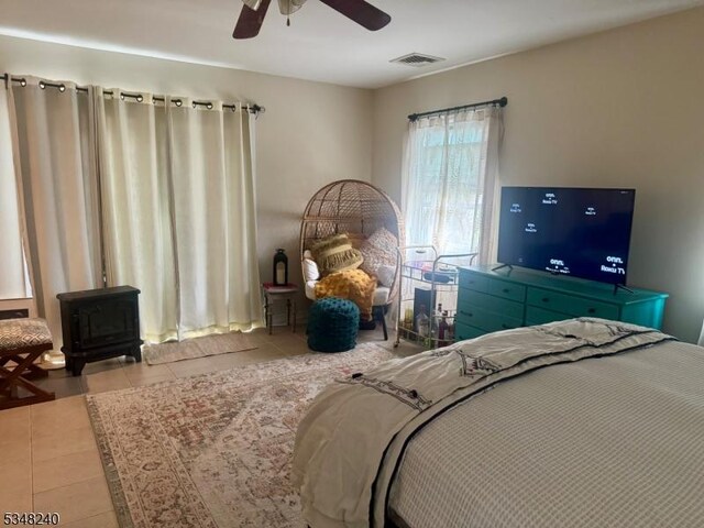 bedroom with a wood stove, visible vents, tile patterned floors, and a ceiling fan