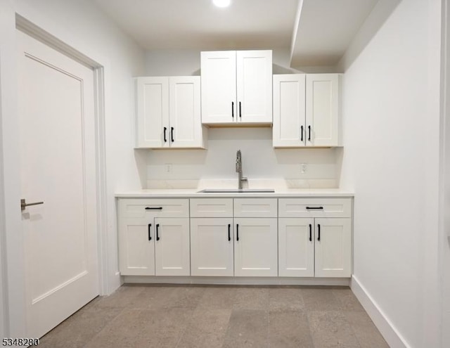 kitchen featuring white cabinets, baseboards, a sink, and light countertops
