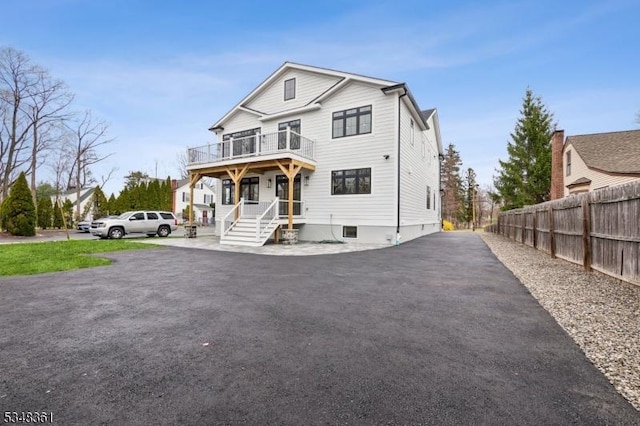 view of front of home featuring driveway, fence, and a balcony