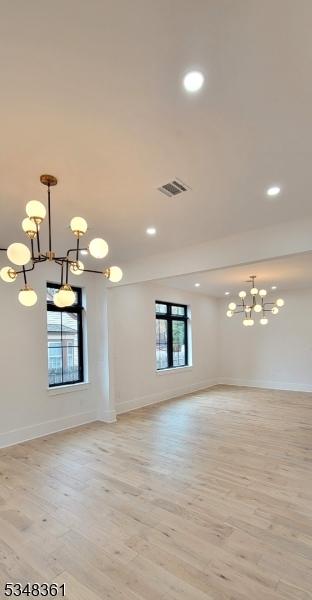 spare room featuring baseboards, visible vents, a notable chandelier, and light wood finished floors