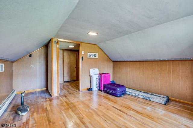 additional living space with a baseboard heating unit, vaulted ceiling, wood walls, and wood finished floors