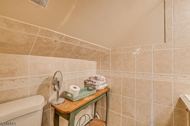 half bathroom with lofted ceiling, tile walls, and toilet