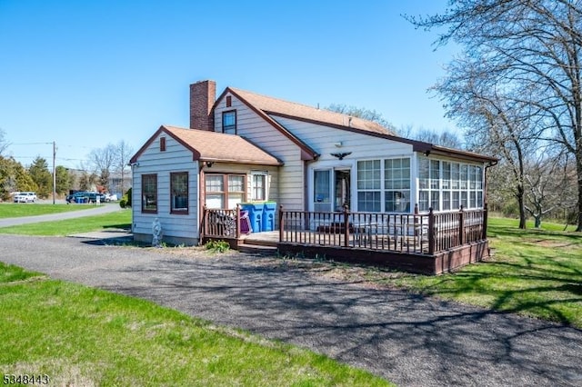 back of house featuring a chimney, a wooden deck, a sunroom, and a lawn