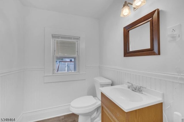 half bathroom featuring vanity, toilet, and a wainscoted wall