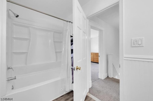 bathroom featuring a wainscoted wall and shower / bathtub combination with curtain