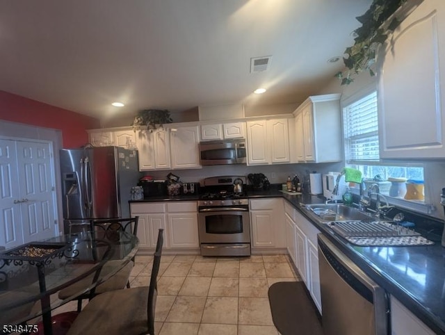 kitchen featuring appliances with stainless steel finishes, dark countertops, white cabinets, a sink, and recessed lighting