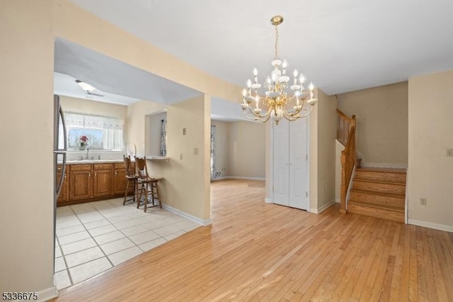 dining space featuring stairs, light wood-style floors, baseboards, and an inviting chandelier
