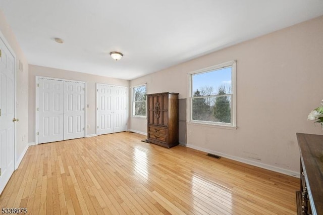 unfurnished bedroom featuring baseboards, multiple closets, visible vents, and light wood-style flooring
