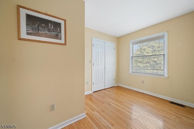 unfurnished bedroom with a closet, hardwood / wood-style flooring, baseboards, and visible vents