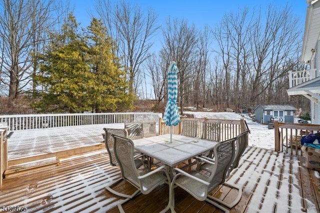 snow covered deck featuring an outdoor structure, a storage unit, and outdoor dining space