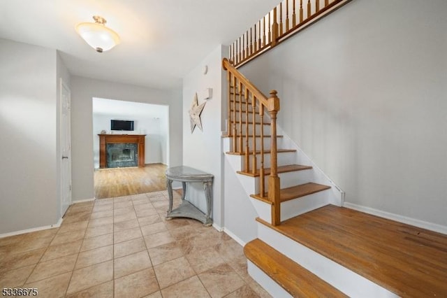 staircase featuring baseboards, a fireplace, and tile patterned flooring