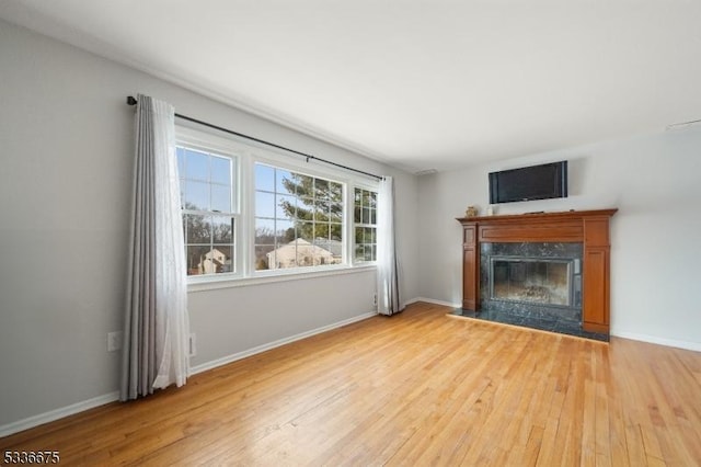 unfurnished living room with a premium fireplace, baseboards, and light wood finished floors