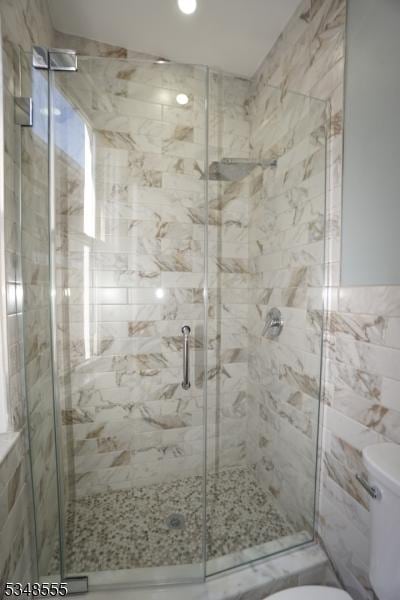 bathroom with a stall shower, tile walls, and toilet