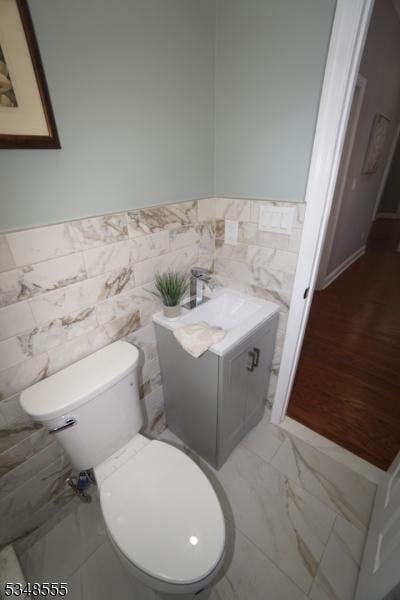 half bath with tile walls, toilet, vanity, wainscoting, and marble finish floor