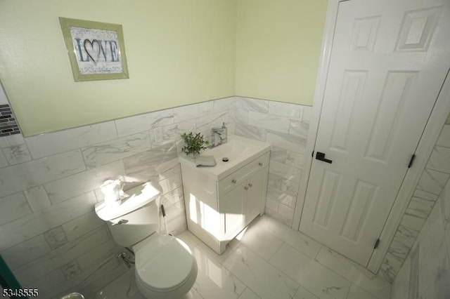 bathroom featuring vanity, tile walls, toilet, wainscoting, and marble finish floor