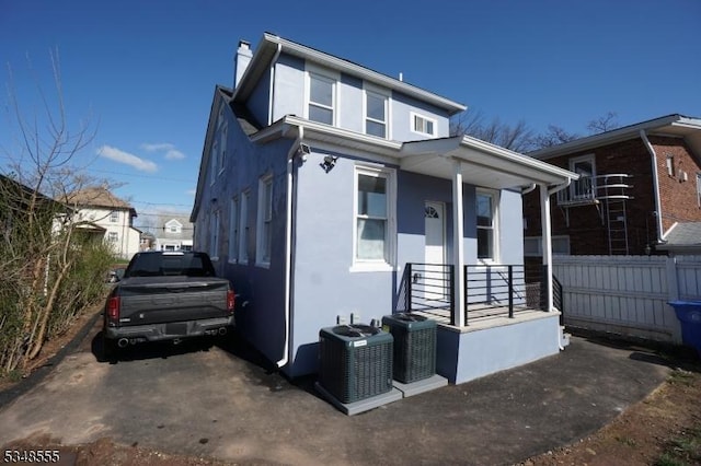 bungalow-style home featuring central AC, covered porch, stucco siding, fence, and a chimney