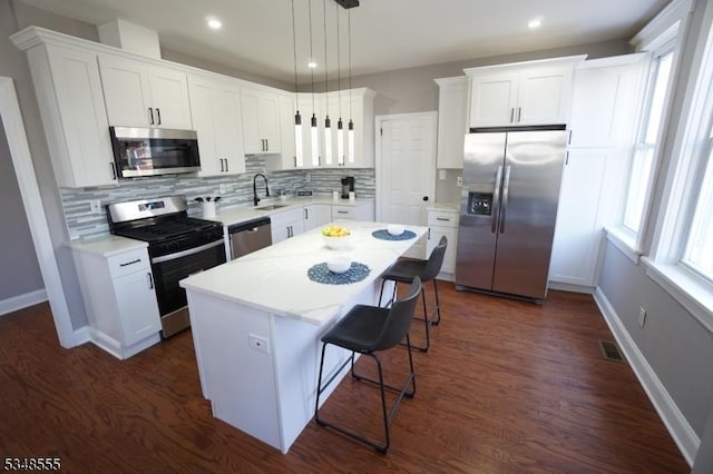 kitchen with white cabinets, a kitchen island, a breakfast bar, appliances with stainless steel finishes, and a sink