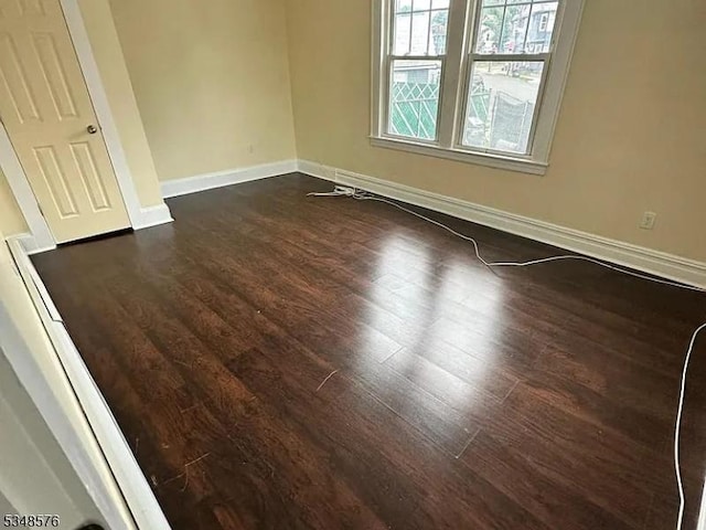 unfurnished room featuring baseboards and dark wood-type flooring