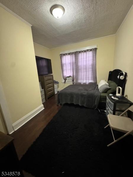 bedroom with baseboards, ornamental molding, wood finished floors, and a textured ceiling