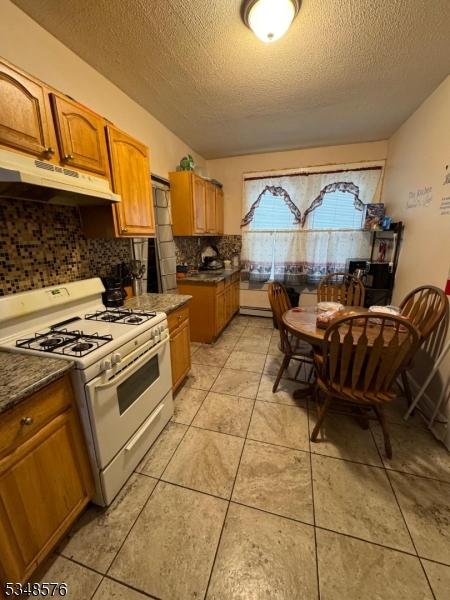 kitchen featuring brown cabinets, under cabinet range hood, white gas range, tasteful backsplash, and a textured ceiling