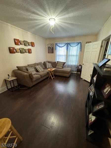 living room with a textured ceiling, ornamental molding, and dark wood-style flooring