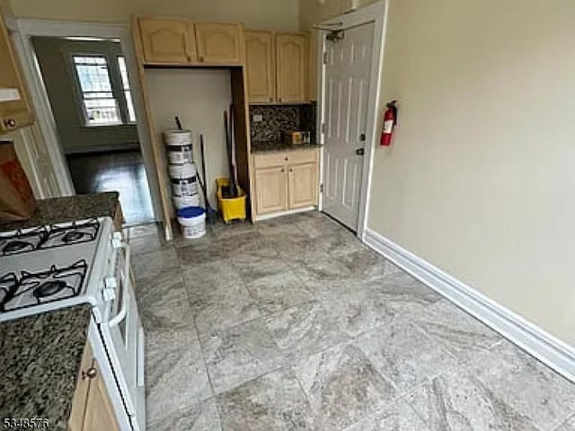 kitchen featuring white range with gas cooktop, baseboards, light brown cabinetry, and tasteful backsplash