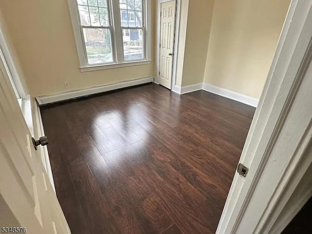 unfurnished room featuring baseboard heating, baseboards, and dark wood-type flooring