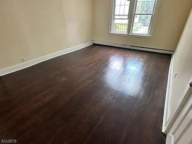 unfurnished room featuring a baseboard heating unit, baseboards, and dark wood-type flooring