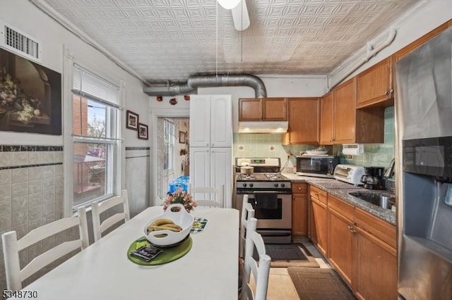 kitchen featuring visible vents, appliances with stainless steel finishes, under cabinet range hood, brown cabinetry, and an ornate ceiling