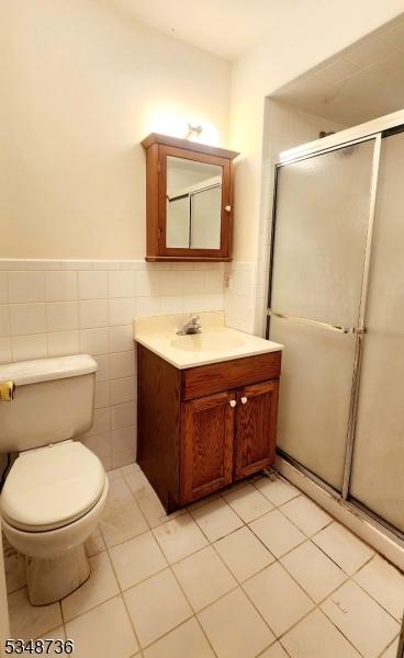 bathroom featuring tile walls, toilet, vanity, and a stall shower