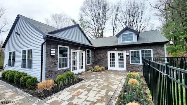 rear view of house featuring stone siding, fence, french doors, and a patio