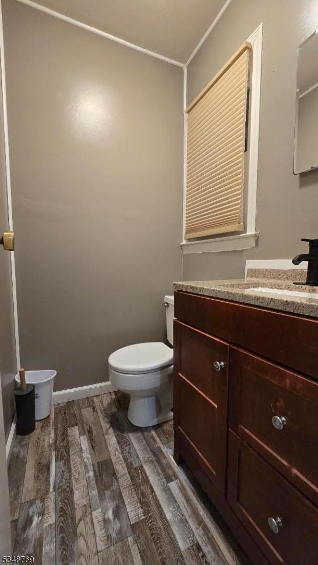 half bathroom with toilet, vanity, and wood finished floors