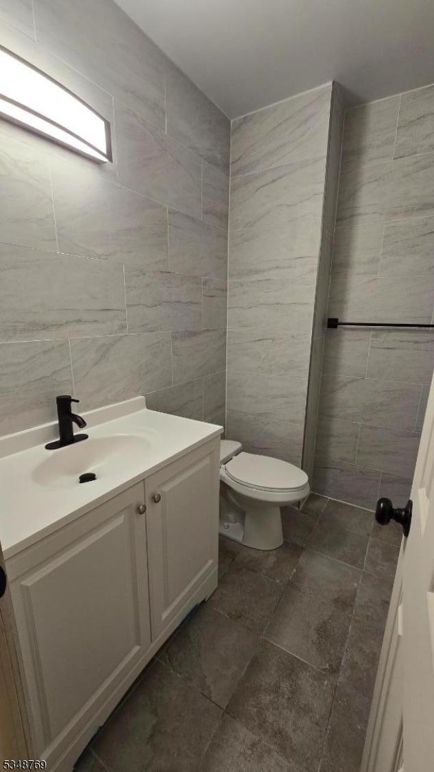 half bathroom featuring toilet, vanity, and tile walls