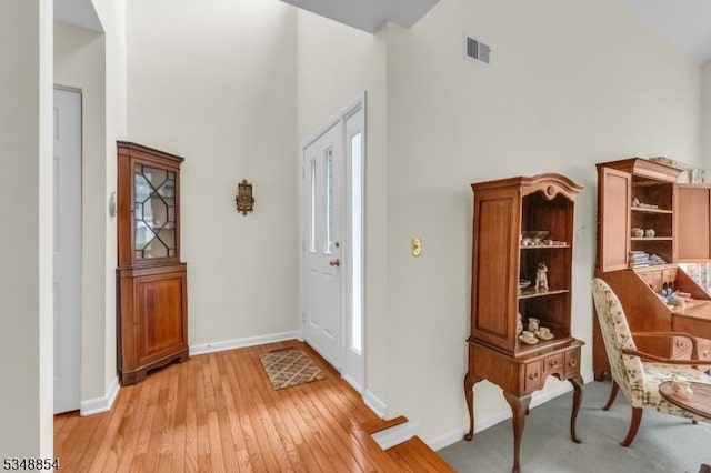 foyer entrance featuring visible vents, baseboards, a high ceiling, and light wood finished floors