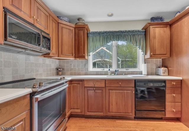 kitchen with brown cabinets, stainless steel appliances, light countertops, a sink, and tasteful backsplash