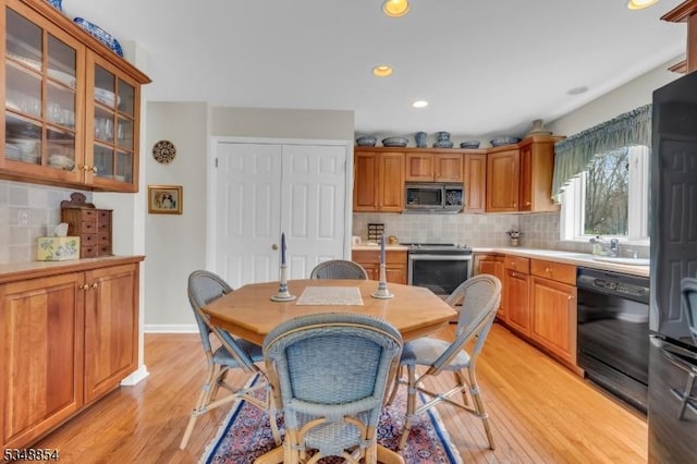 kitchen featuring black appliances, tasteful backsplash, light wood finished floors, and light countertops