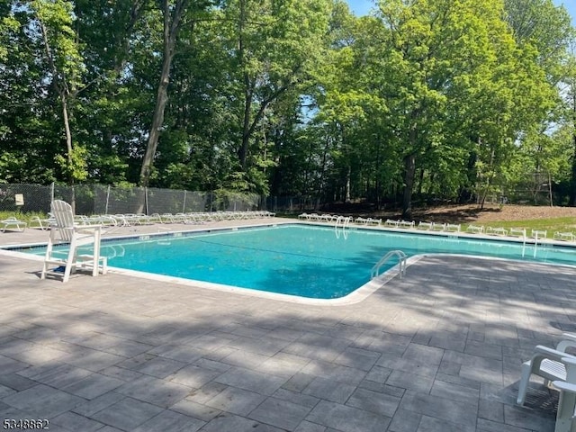 community pool featuring a patio, fence, and view of wooded area