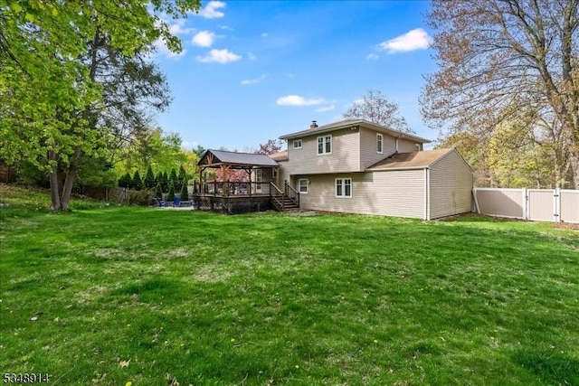rear view of house with a lawn, a wooden deck, a fenced backyard, a gate, and a gazebo