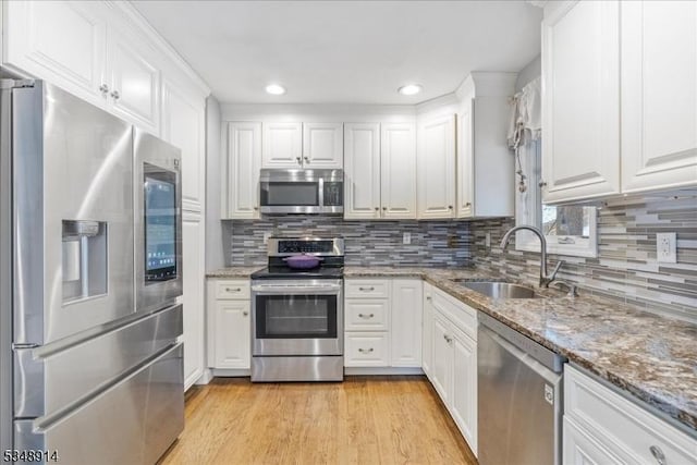 kitchen with light wood-type flooring, white cabinetry, tasteful backsplash, a sink, and stainless steel appliances