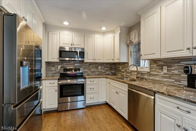 kitchen featuring appliances with stainless steel finishes, a sink, dark stone countertops, recessed lighting, and white cabinetry