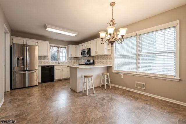 kitchen with a notable chandelier, appliances with stainless steel finishes, white cabinetry, decorative backsplash, and visible vents