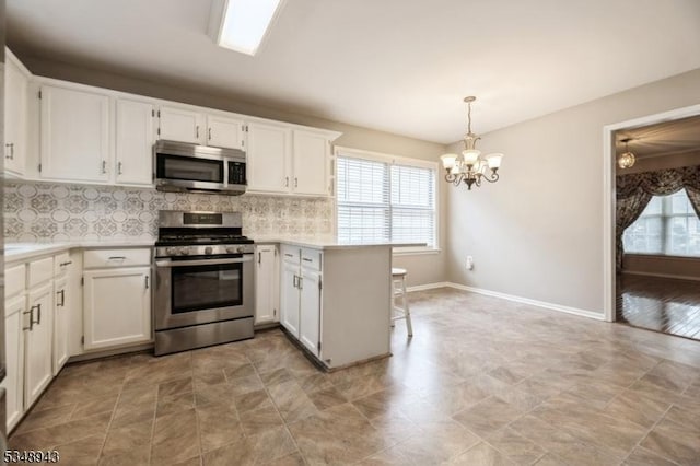 kitchen featuring backsplash, light countertops, a peninsula, an inviting chandelier, and stainless steel appliances