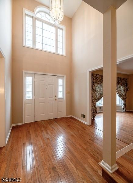 entrance foyer with wood-type flooring, baseboards, a towering ceiling, and a notable chandelier