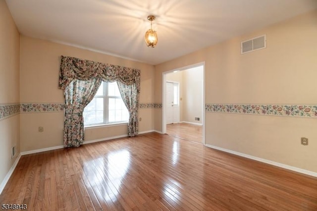 unfurnished room with baseboards, wood finished floors, and visible vents