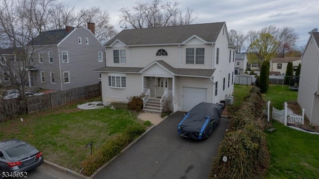 traditional-style house featuring driveway, a garage, fence, and a front lawn