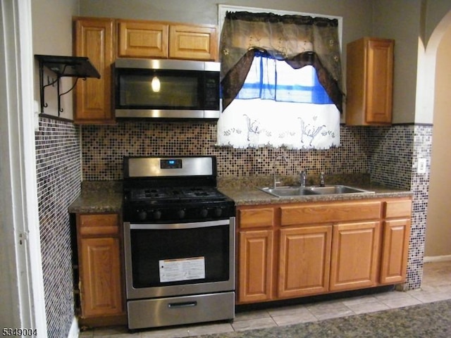 kitchen with arched walkways, tasteful backsplash, a sink, light tile patterned floors, and stainless steel appliances