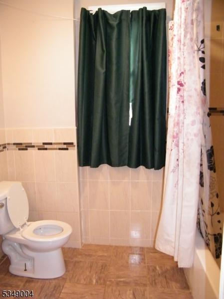 full bath featuring toilet and tile walls