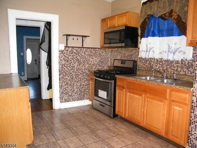kitchen with appliances with stainless steel finishes, dark countertops, tasteful backsplash, a sink, and light tile patterned floors