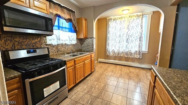 kitchen with light tile patterned flooring, a baseboard radiator, a sink, backsplash, and stainless steel appliances